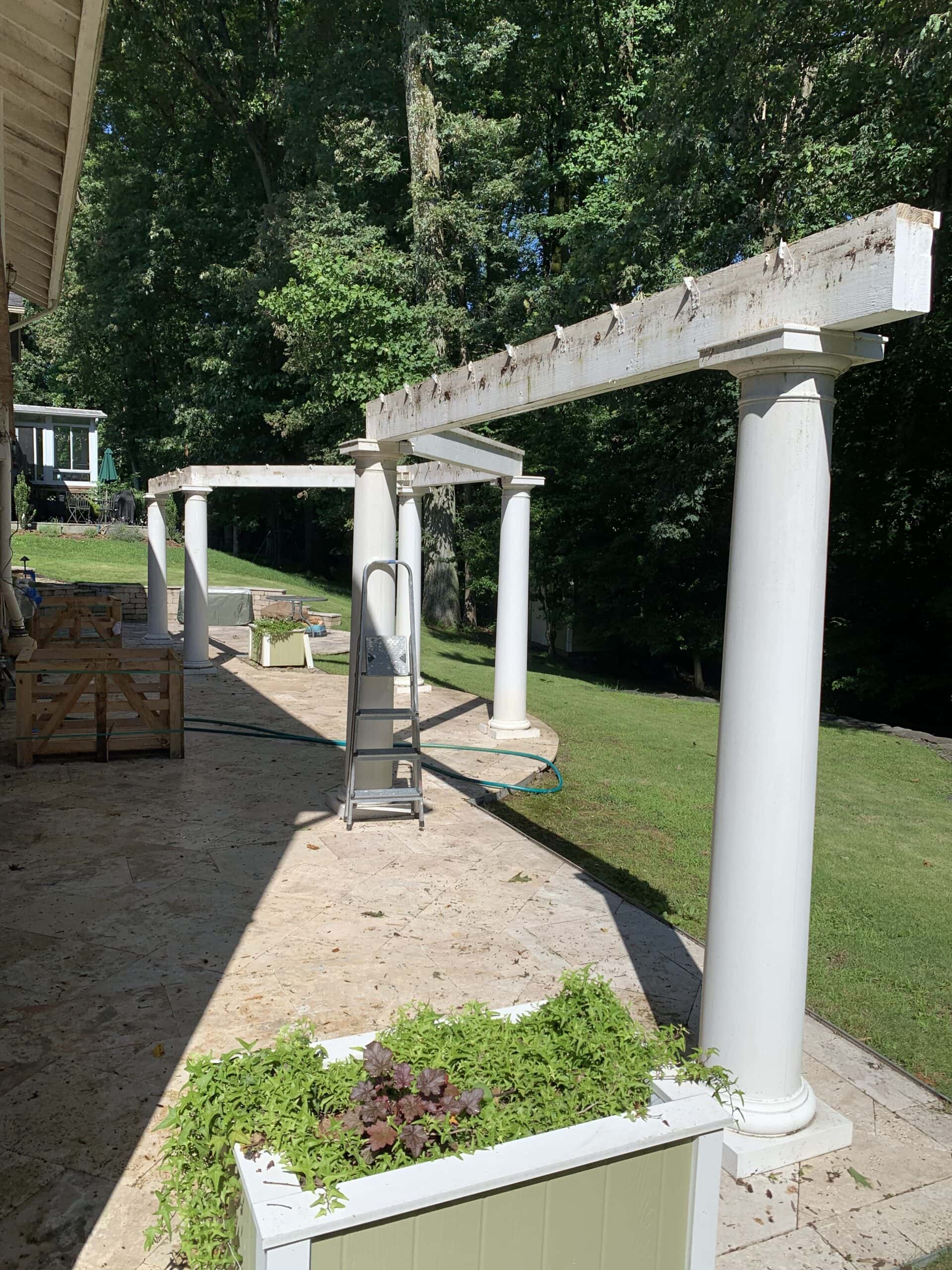 A patio with white columns and a planter.