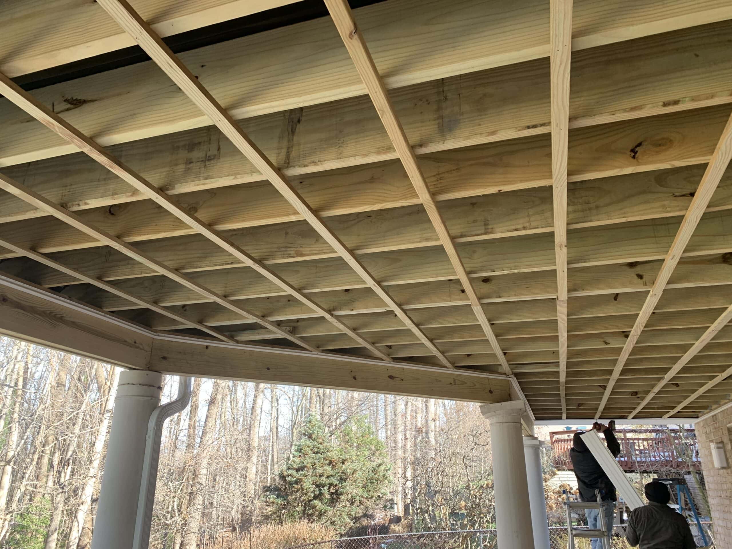 A man is working on a porch with a wooden ceiling.