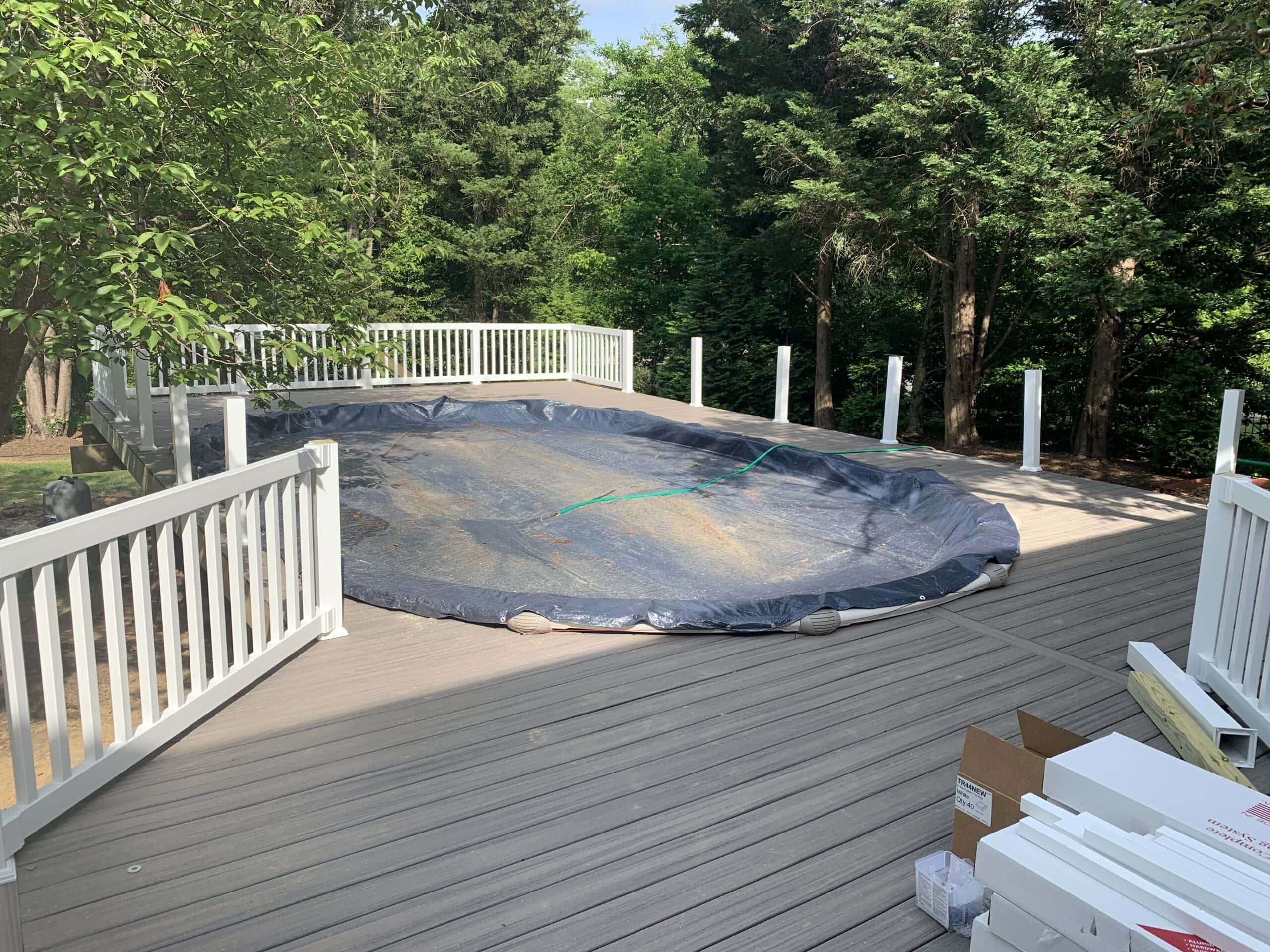 Trex deck partially completed with pool covered and white PVC railings installed