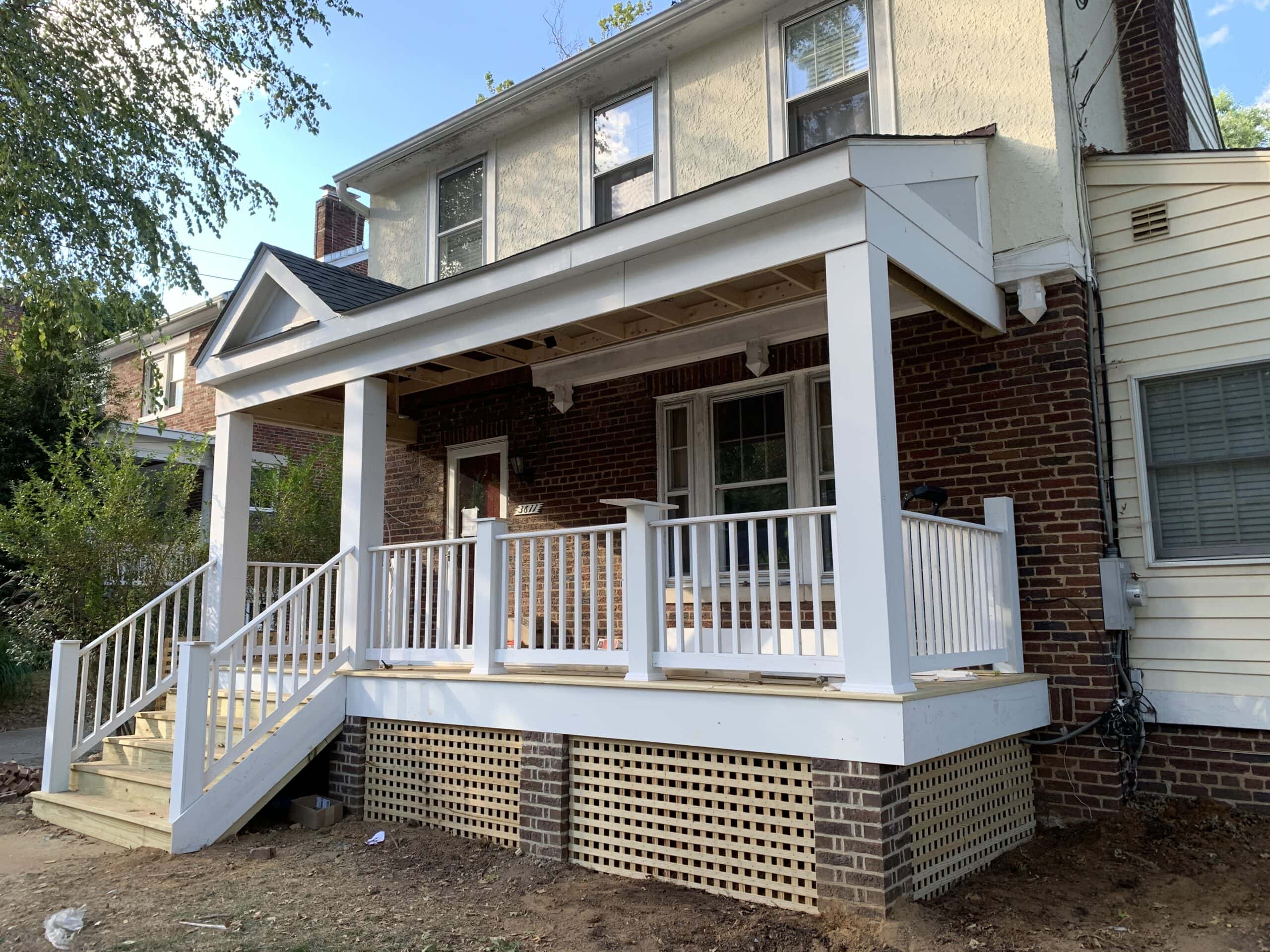 Nearly completed front porch with white railings, columns, and brick foundation.