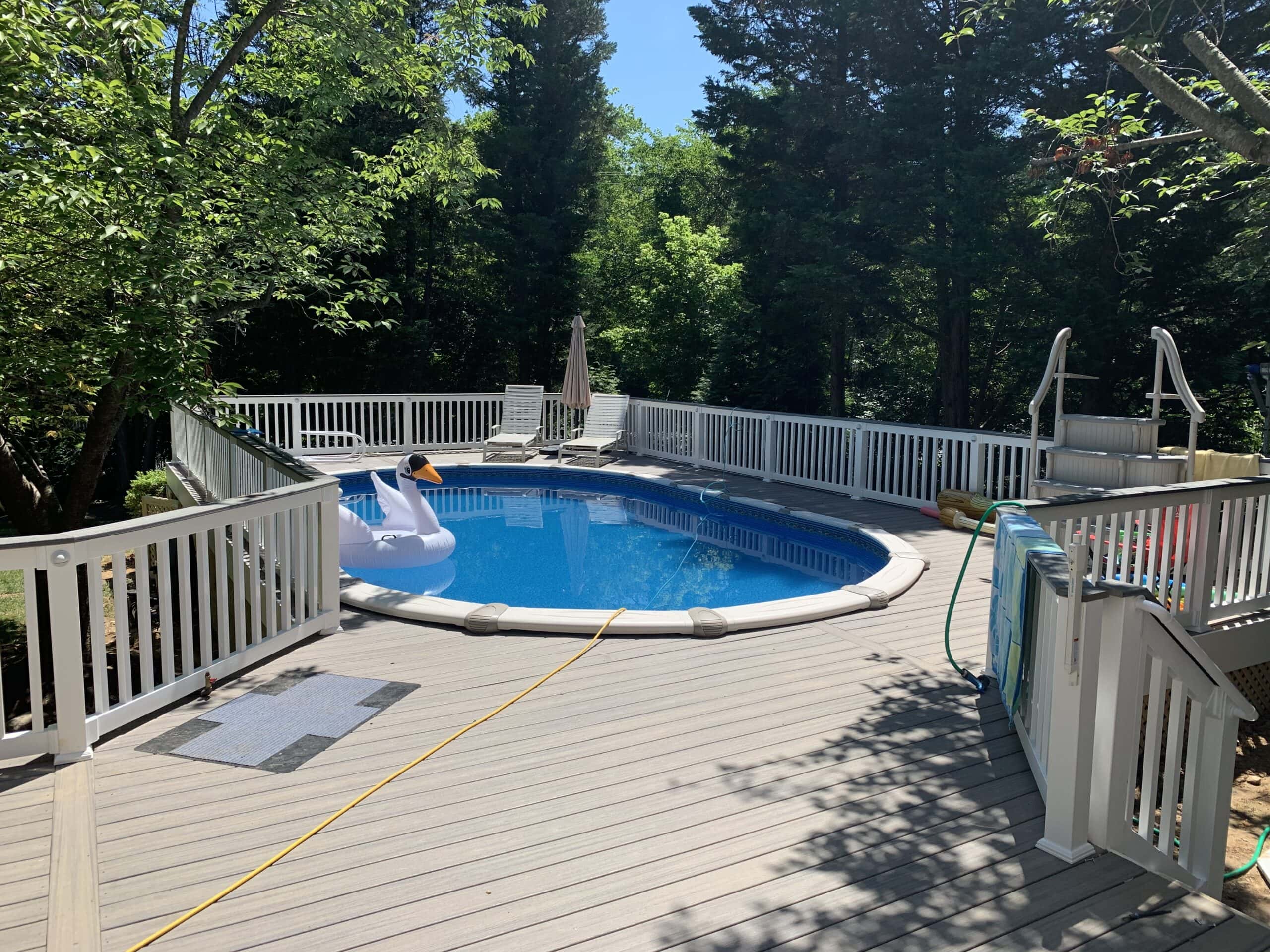 Above-ground pool surrounded by finished Trex deck with white PVC railings and safety features