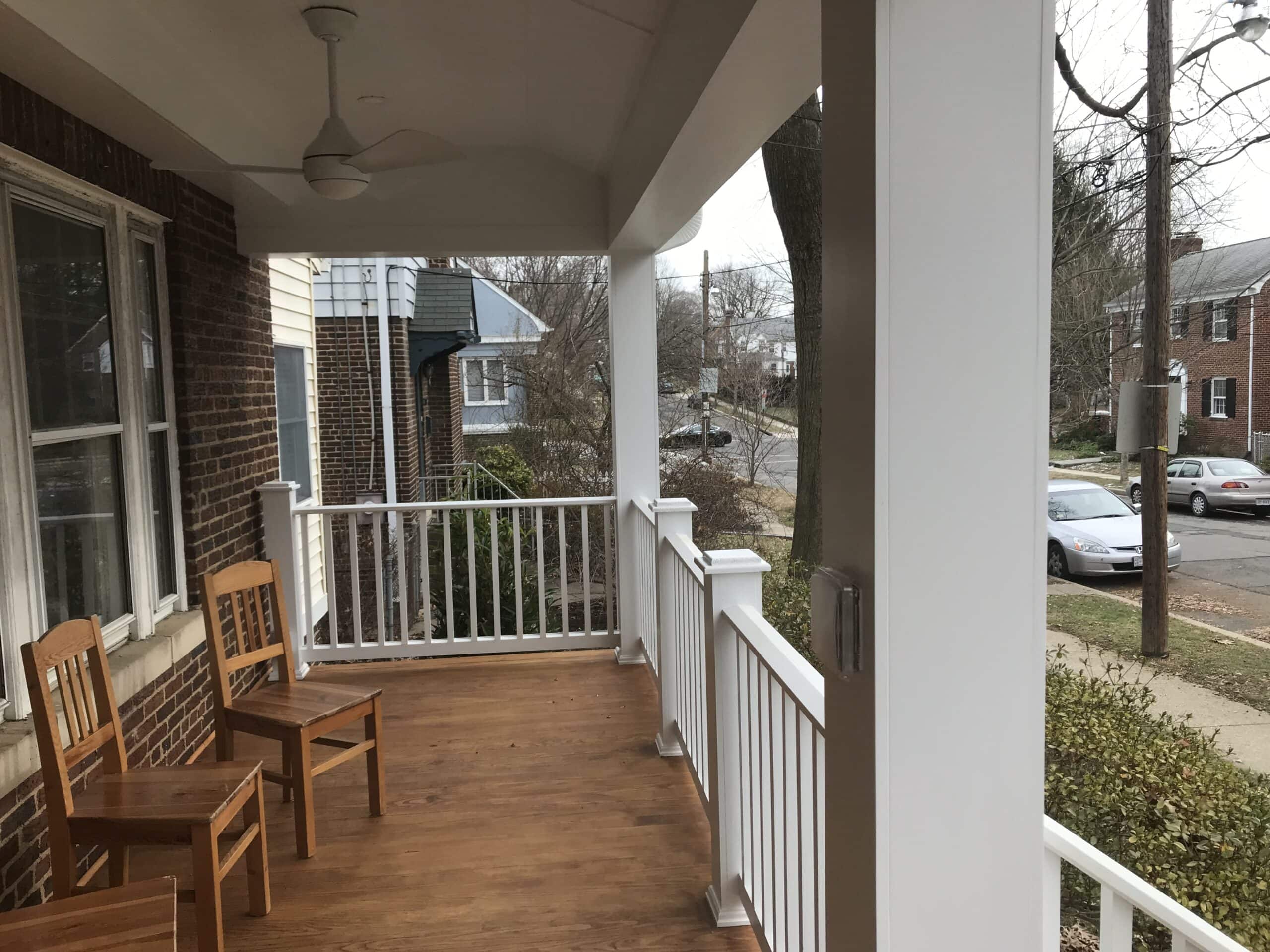 A porch with two wooden chairs and a fan.