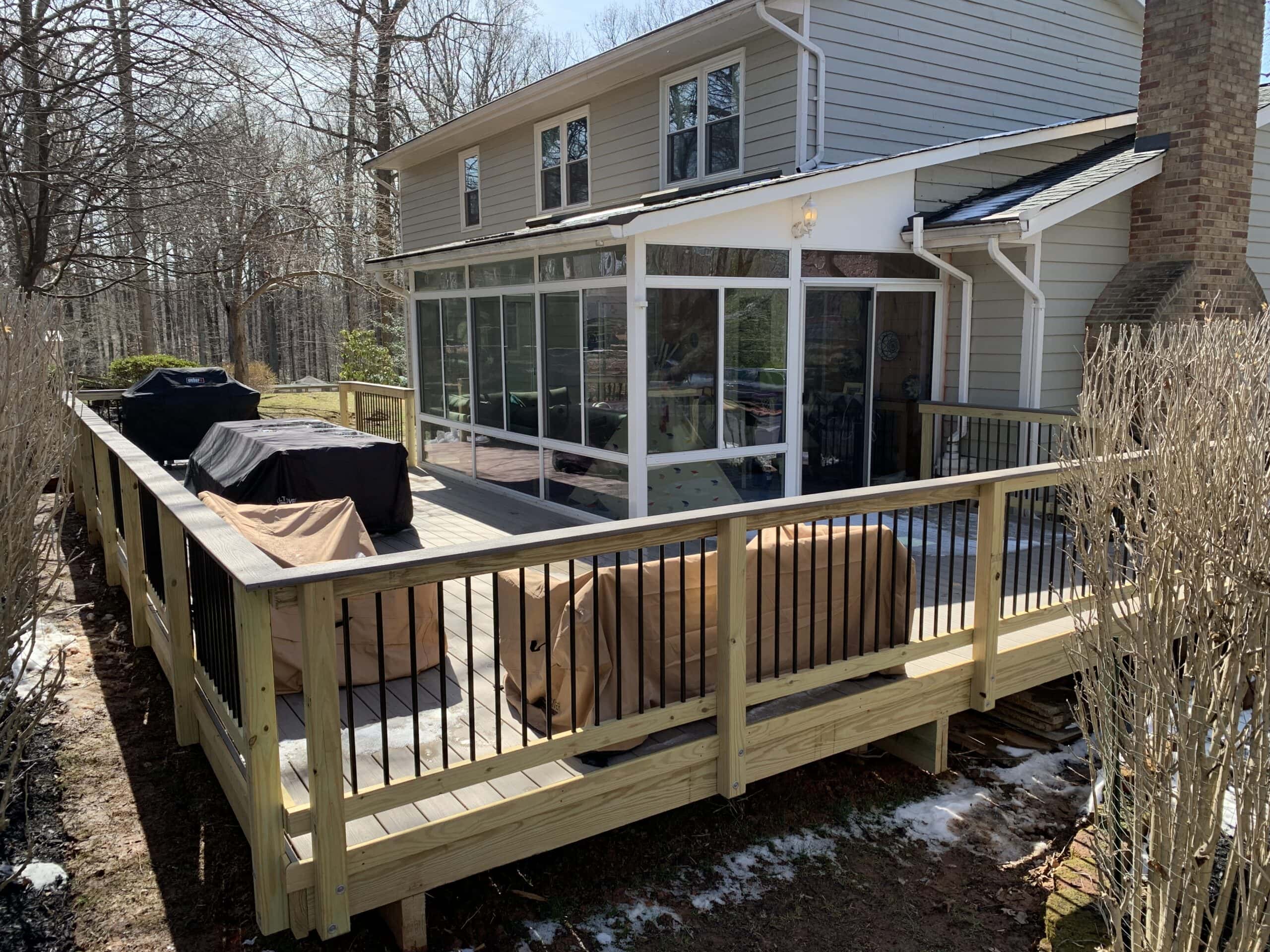 A deck with a screened in porch and a grill.