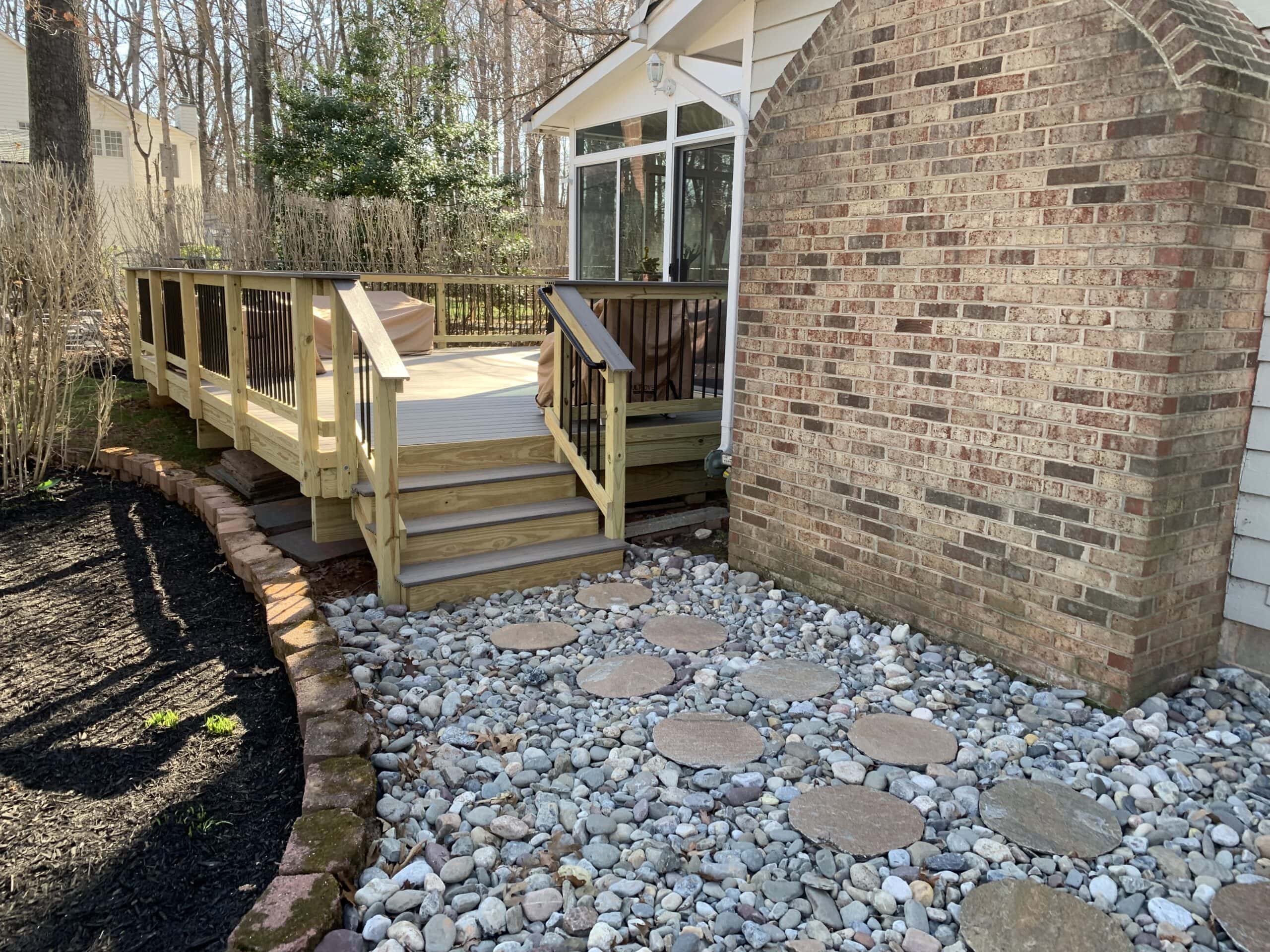 A backyard with a deck and steps leading to a brick patio.