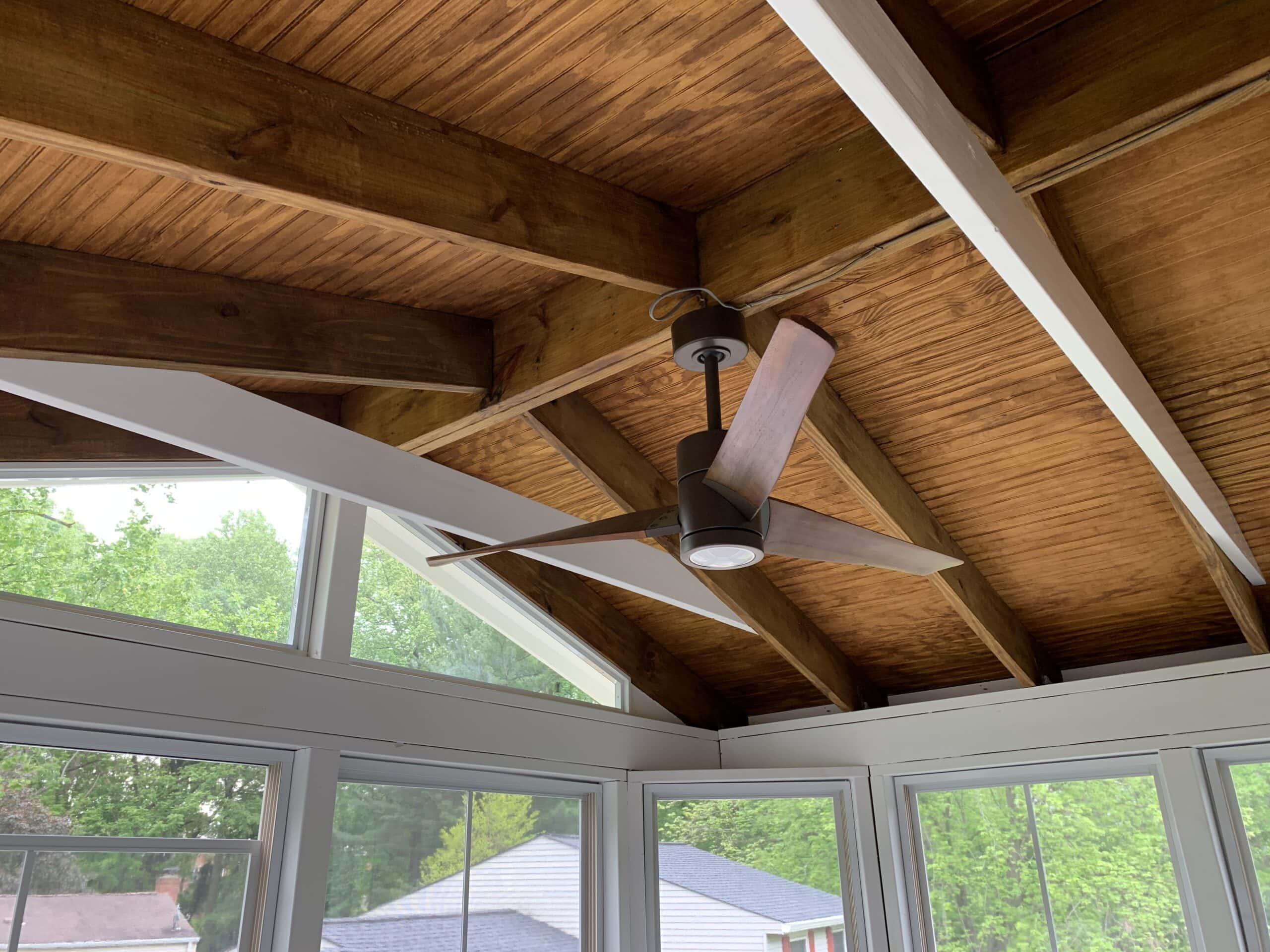 A sunroom with a ceiling fan and wooden beams.