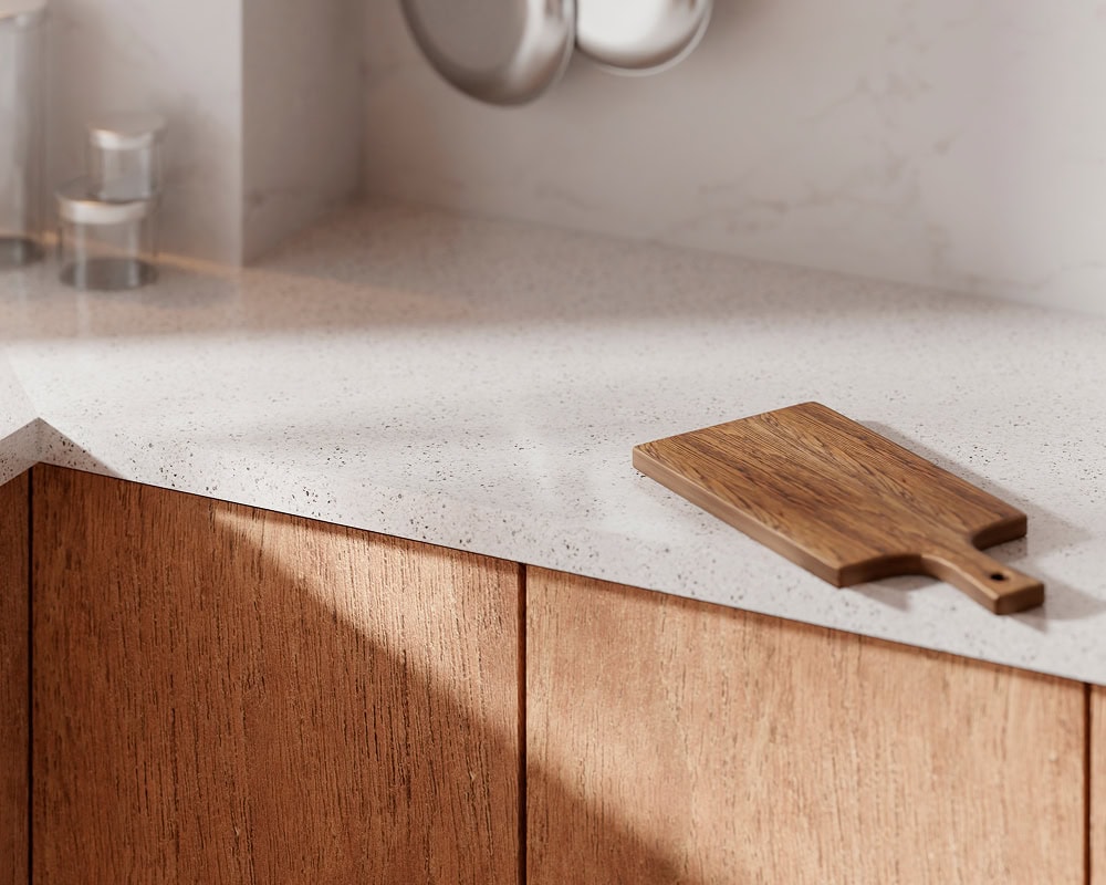 A wooden cutting board rests on a light-colored, speckled kitchen countertop with wooden cabinets below and a marble backsplash in the background—showcasing the elegant touch of a skilled kitchen remodeling contractor.