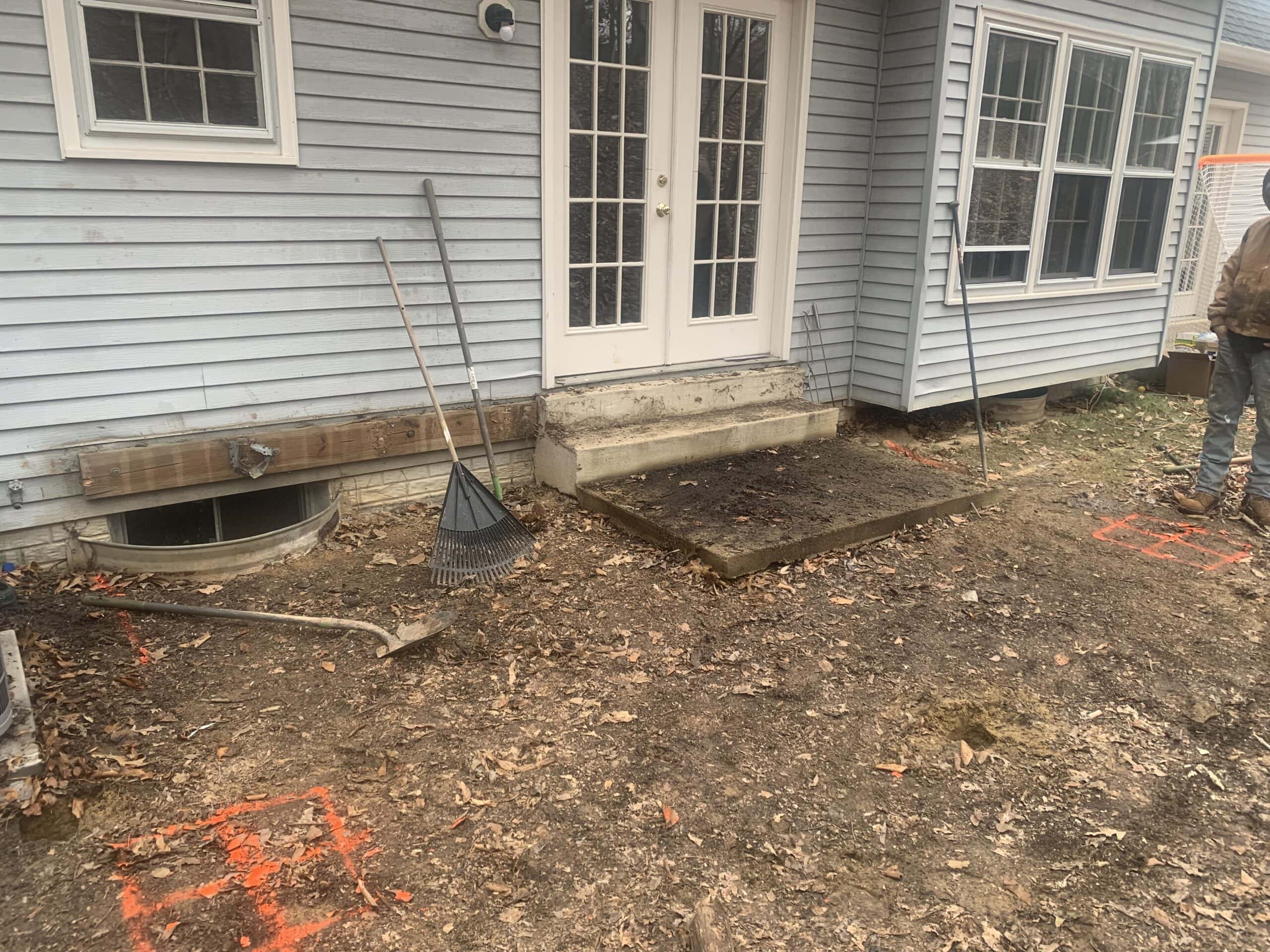 View of the original steep backyard with an outdated patio door and uneven ground before construction began