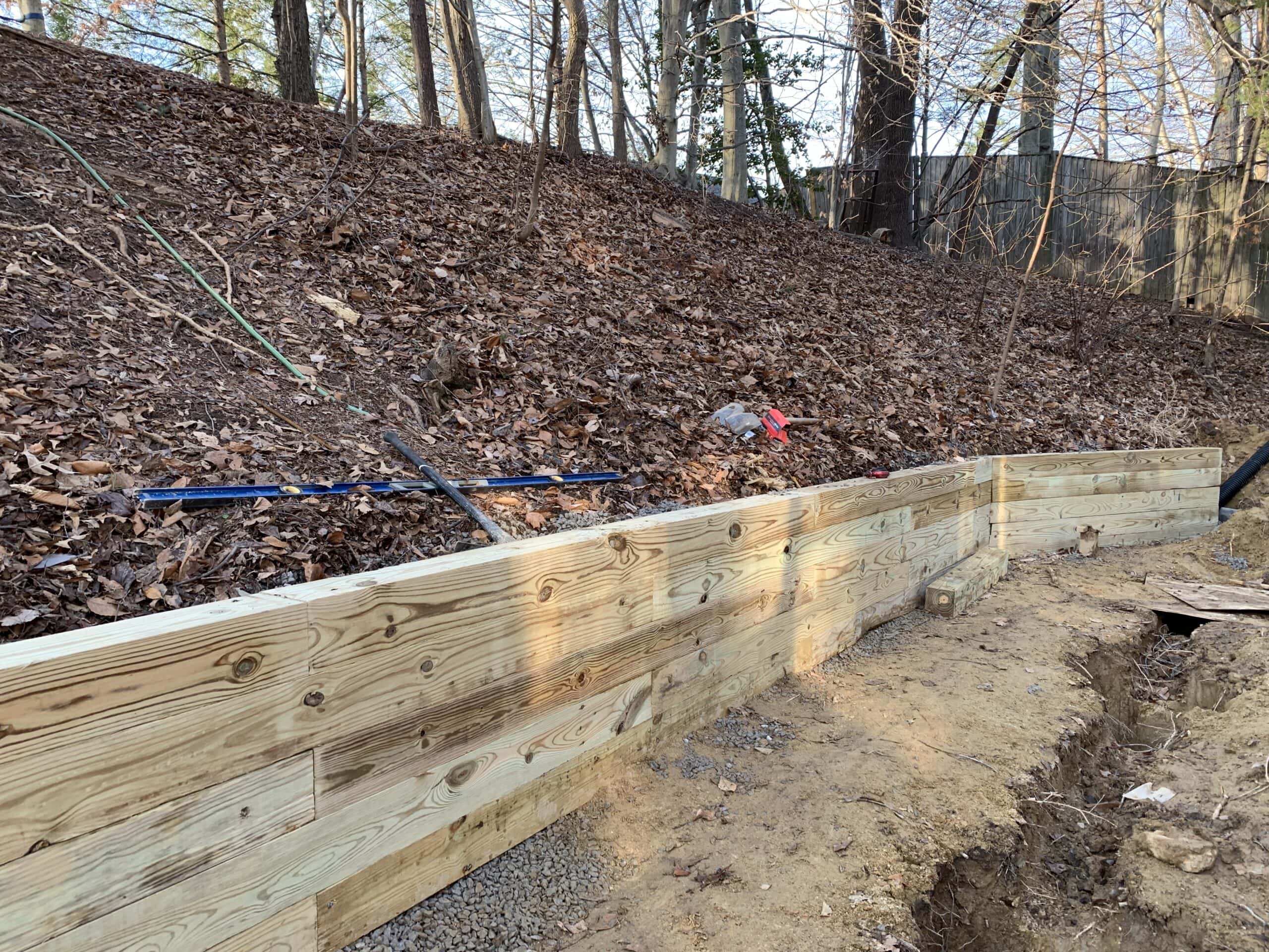Pressure-treated retaining wall partially installed along the slope, preparing for deck framing.