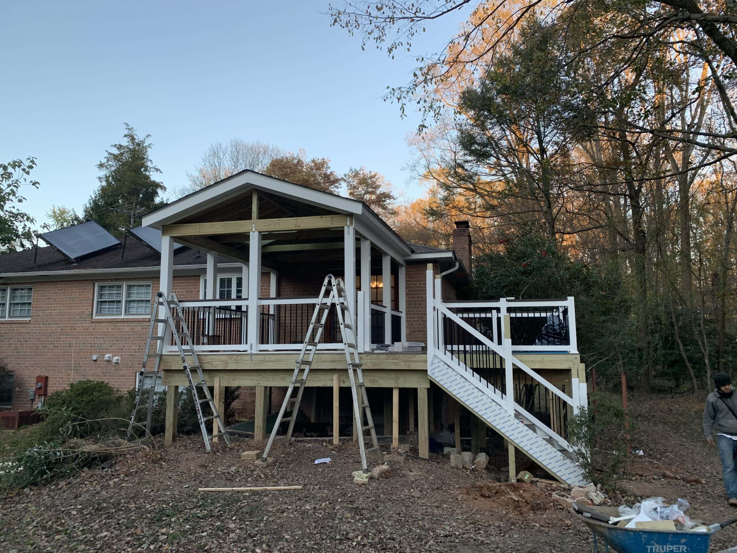 New three-season room and deck framework mostly complete, with stairs and vinyl railing installation underway.