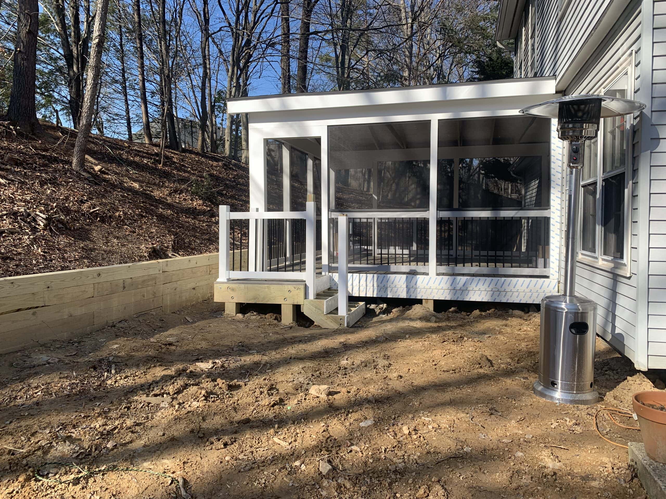 Completed screened-in porch with white trim and black balusters, neatly anchored by the retaining wall.