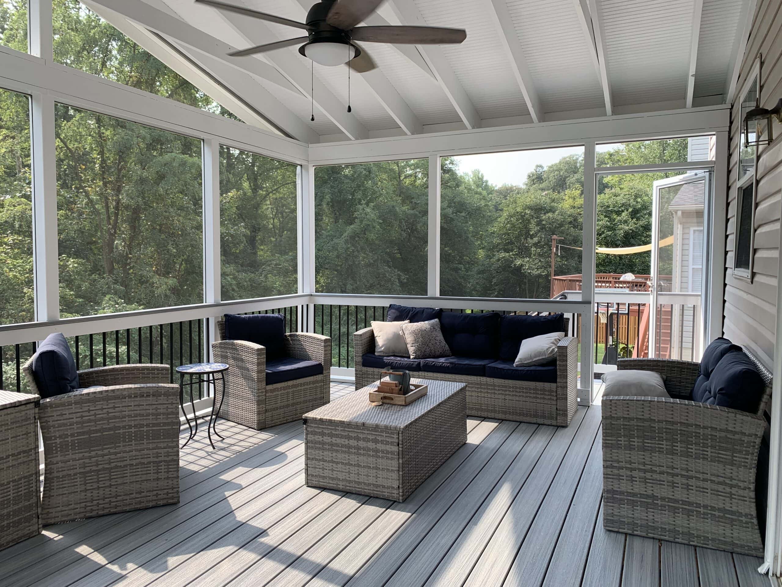 A screened porch featuring wicker furniture and a ceiling fan, designed for comfort and functionality on a steep slope.