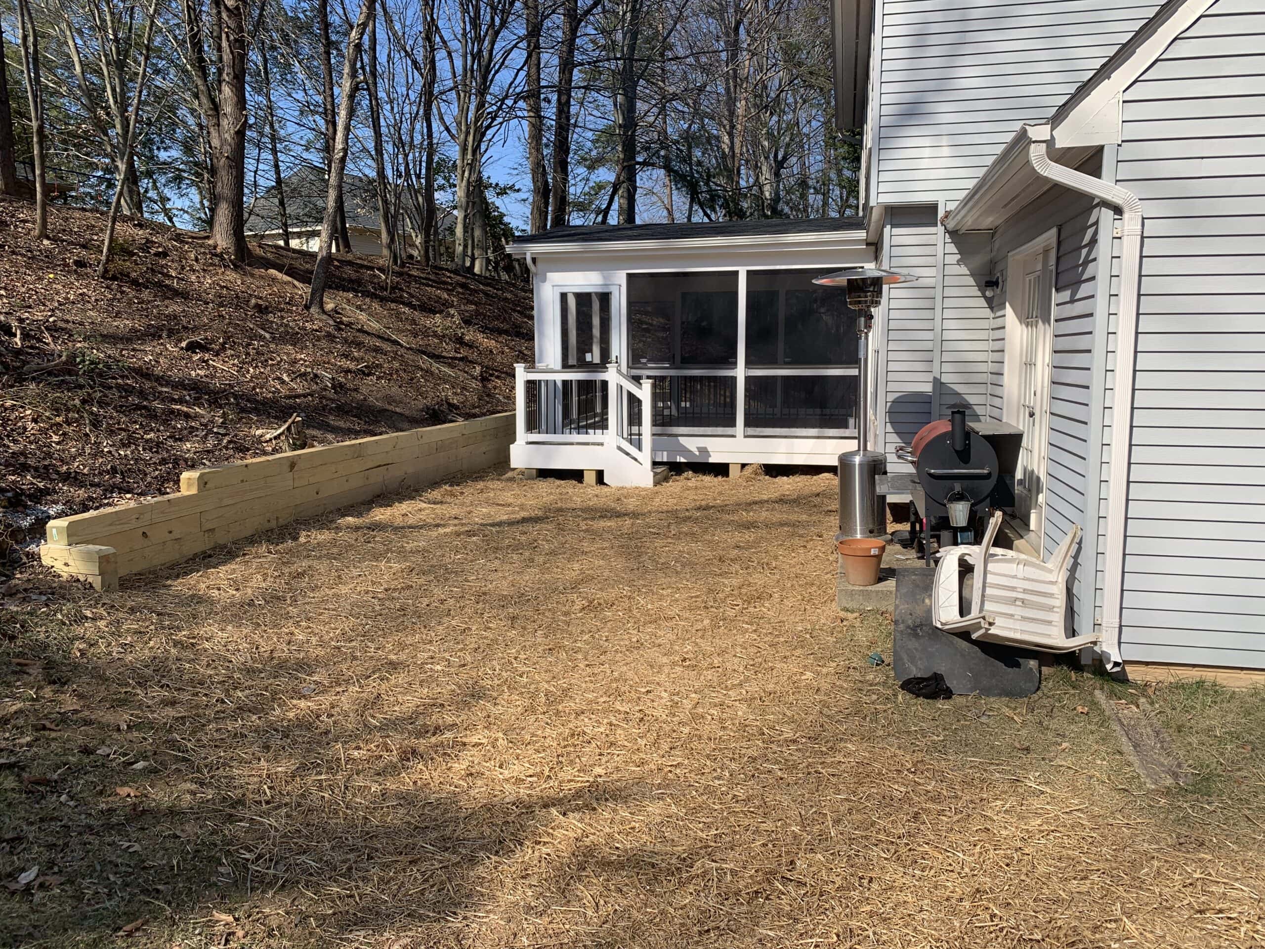 Completed screened-in porch with white trim and black balusters, neatly anchored by the retaining wall.